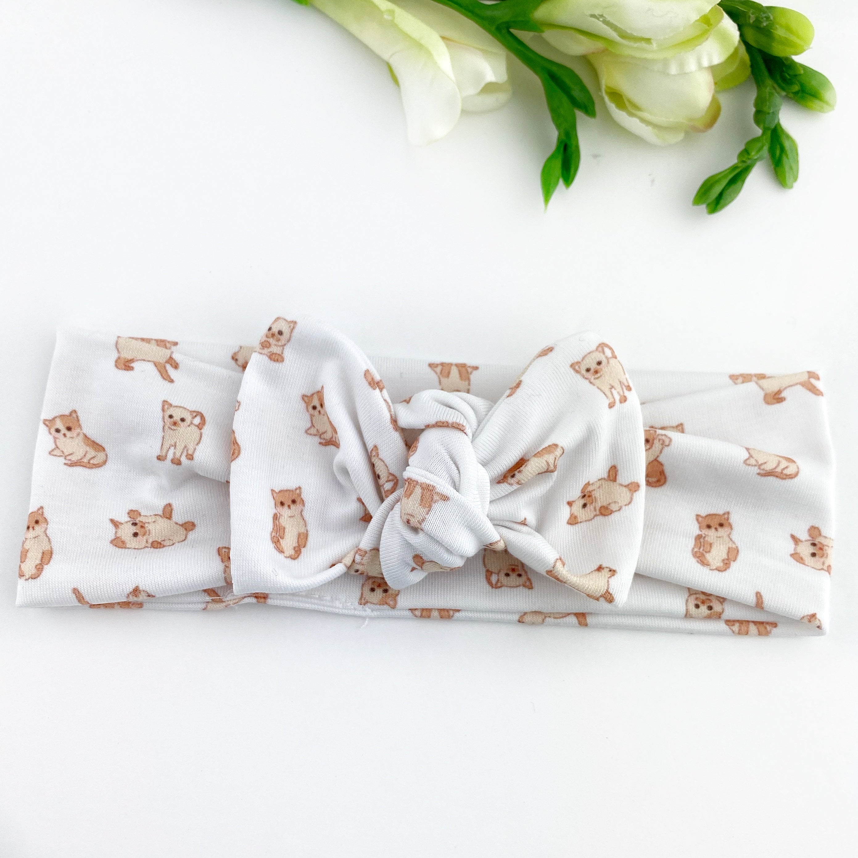 A white top knot baby headband with a kitten pattern