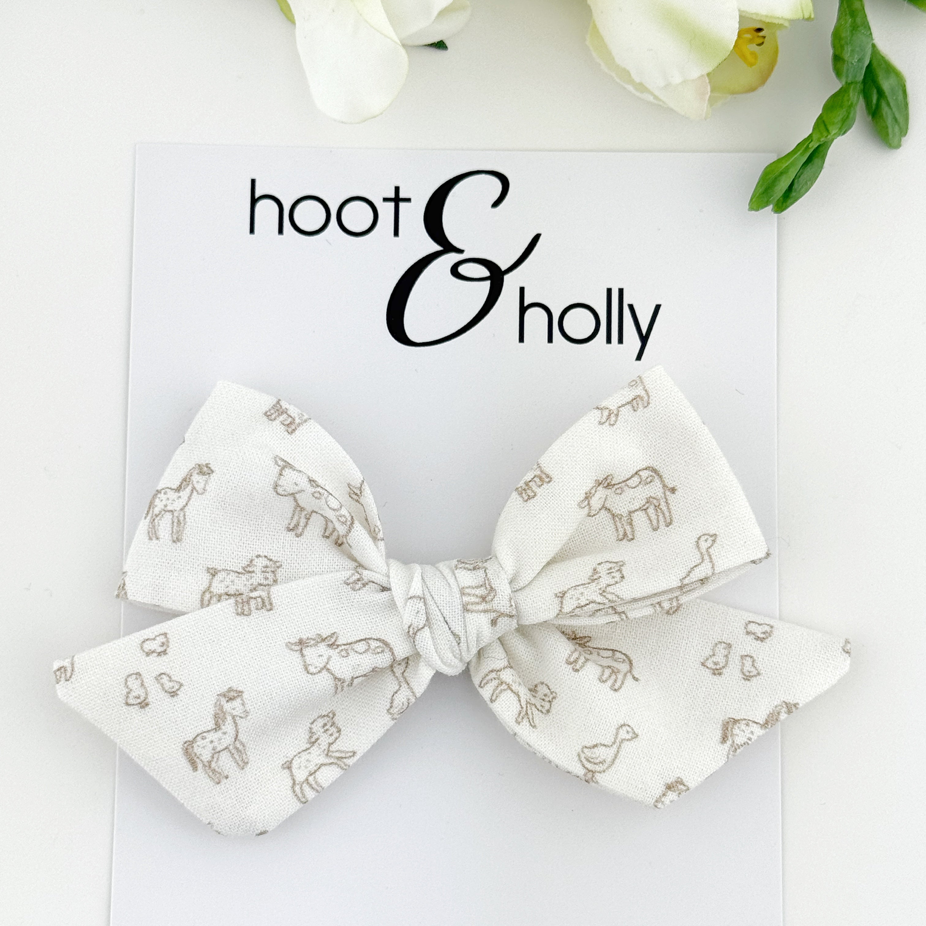 White bow with farm animal pattern on a white card with 'hoot & holly' branding