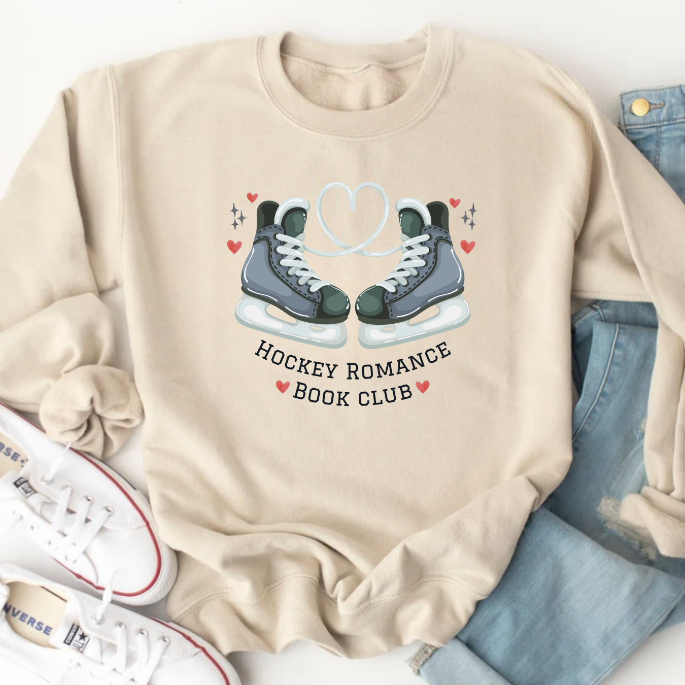 Beige sweatshirt with hockey skates and 'Hockey Romance Book Club' text, surrounded by jeans and sneakers.