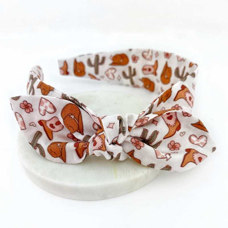 Girls knot bow headband with a cowgirl love theme, featuring motifs like horses and hearts.