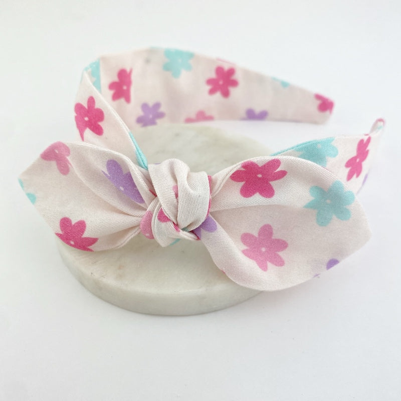 Girls headband with multicolored daisy patterns on a white background.