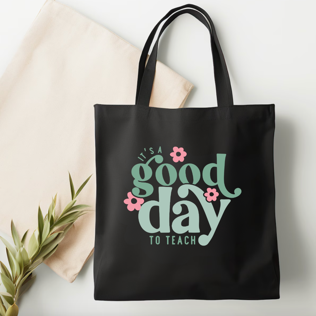 Black tote bag with 'It's a good day to teach' text and flowers on a light background