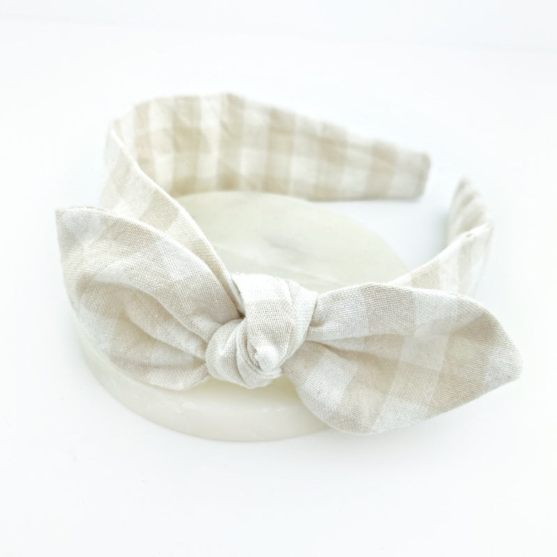 An ivory gingham knot bow headband with plastic covered in fabric, designed for children and small adults.