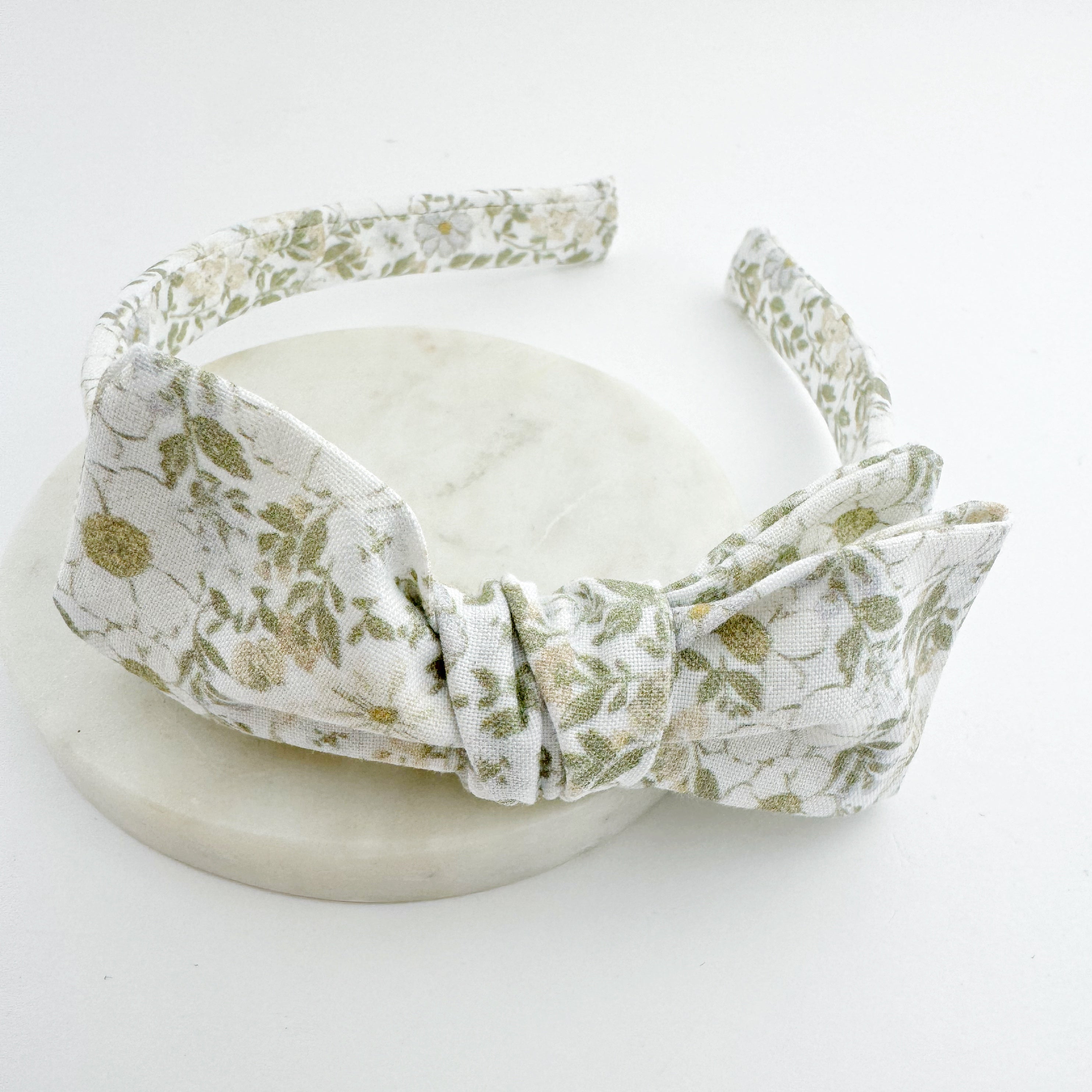 A floral patterned bow headband displayed on a white stand
