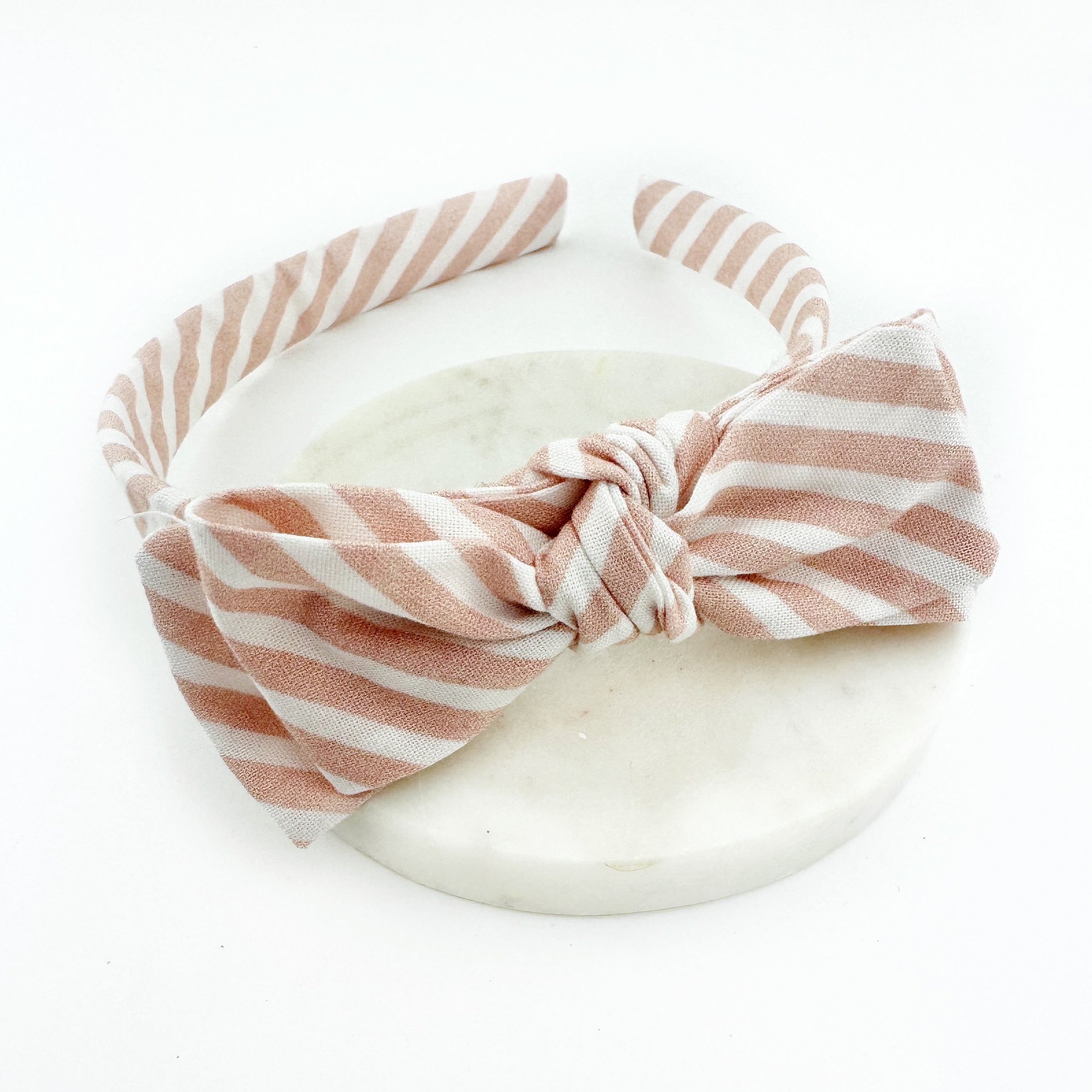 A pink and white striped bow headband presented on a neutral background.