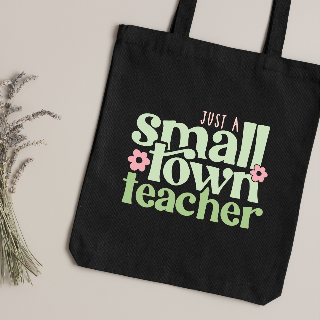 Black tote bag with 'Just a small town teacher' text on a light background