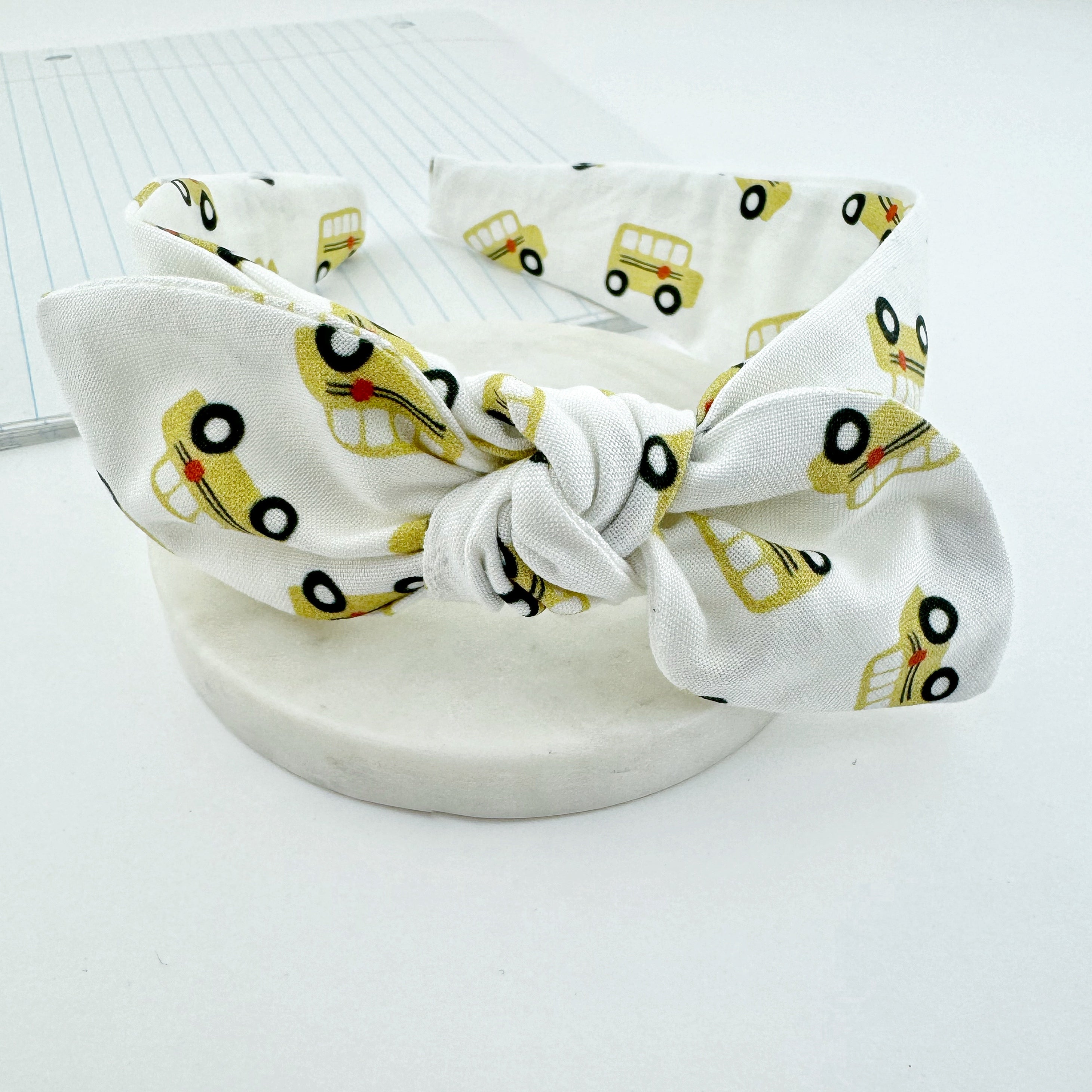 Girls knot how headband featuring a repeated pattern of school buses.