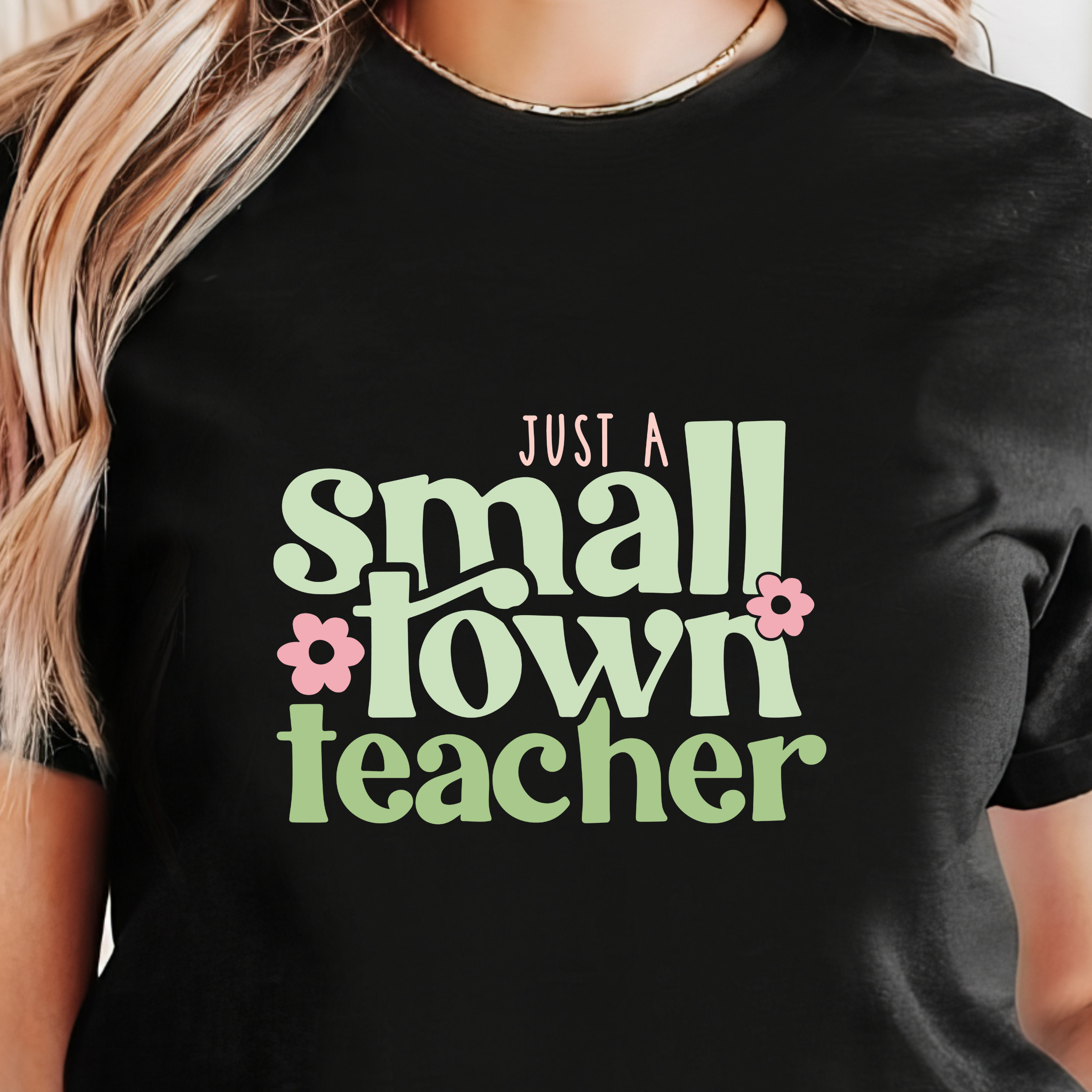 Black t-shirt with 'Just a small town teacher' text in green and pink flowers worn by a person.