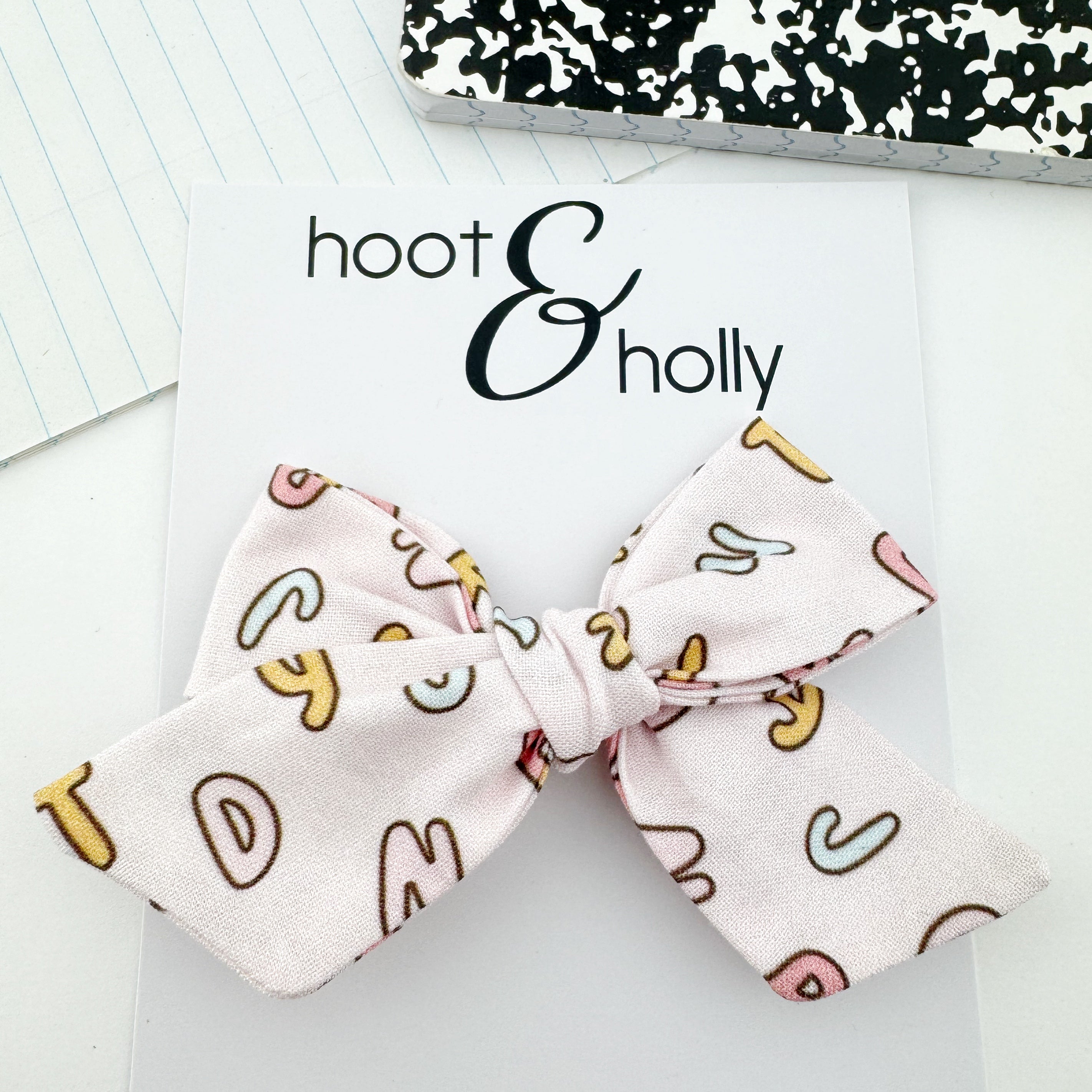 Hand-tied hair bow with alphabet pattern on pink.