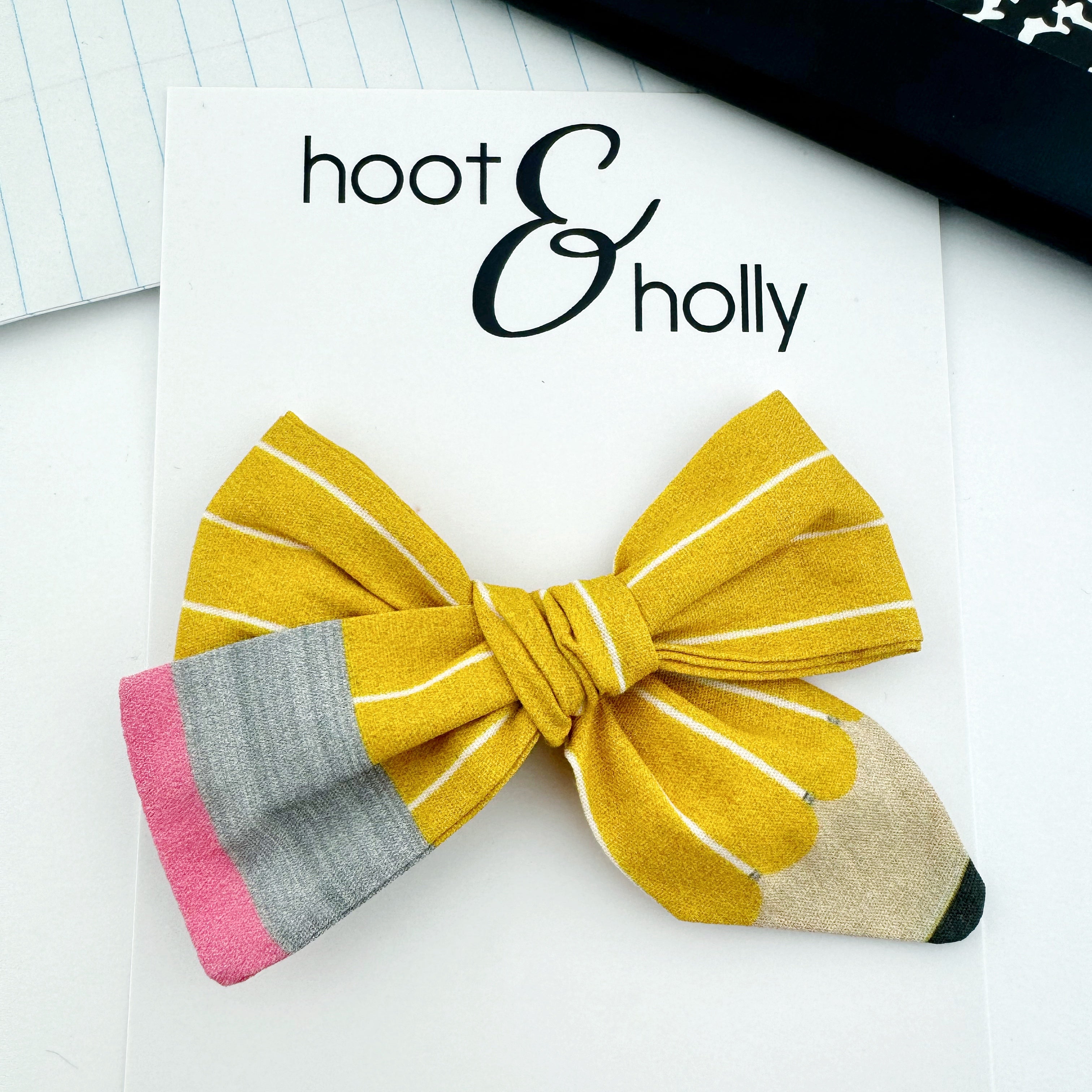 A hand-tied cotton hair bow with a pencil design, featuring yellow and gray stripes.