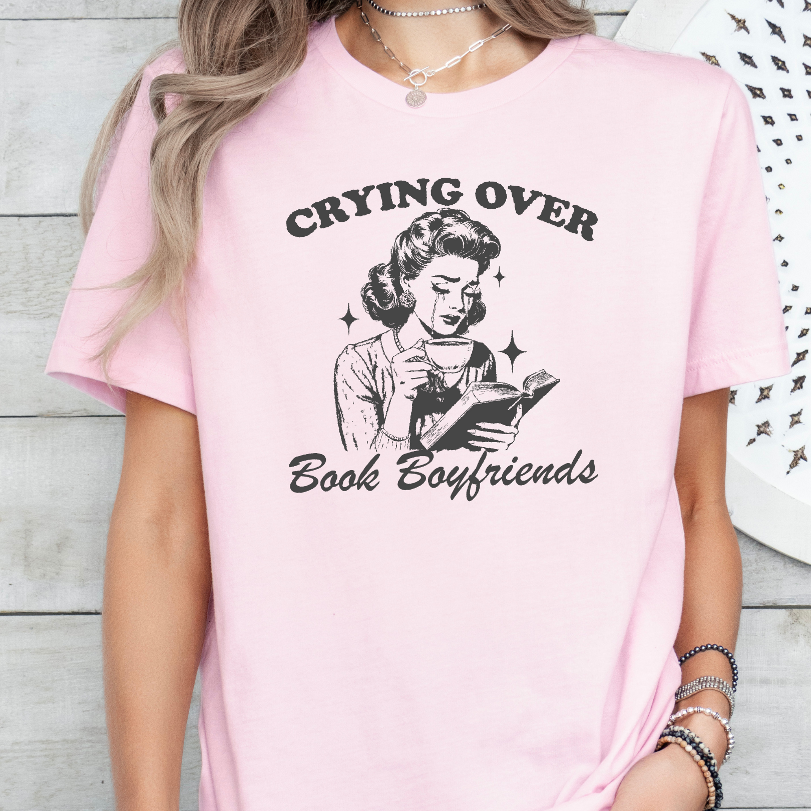 Pink t-shirt with graphic and text 'Crying Over Book Boyfriends' worn by a person.