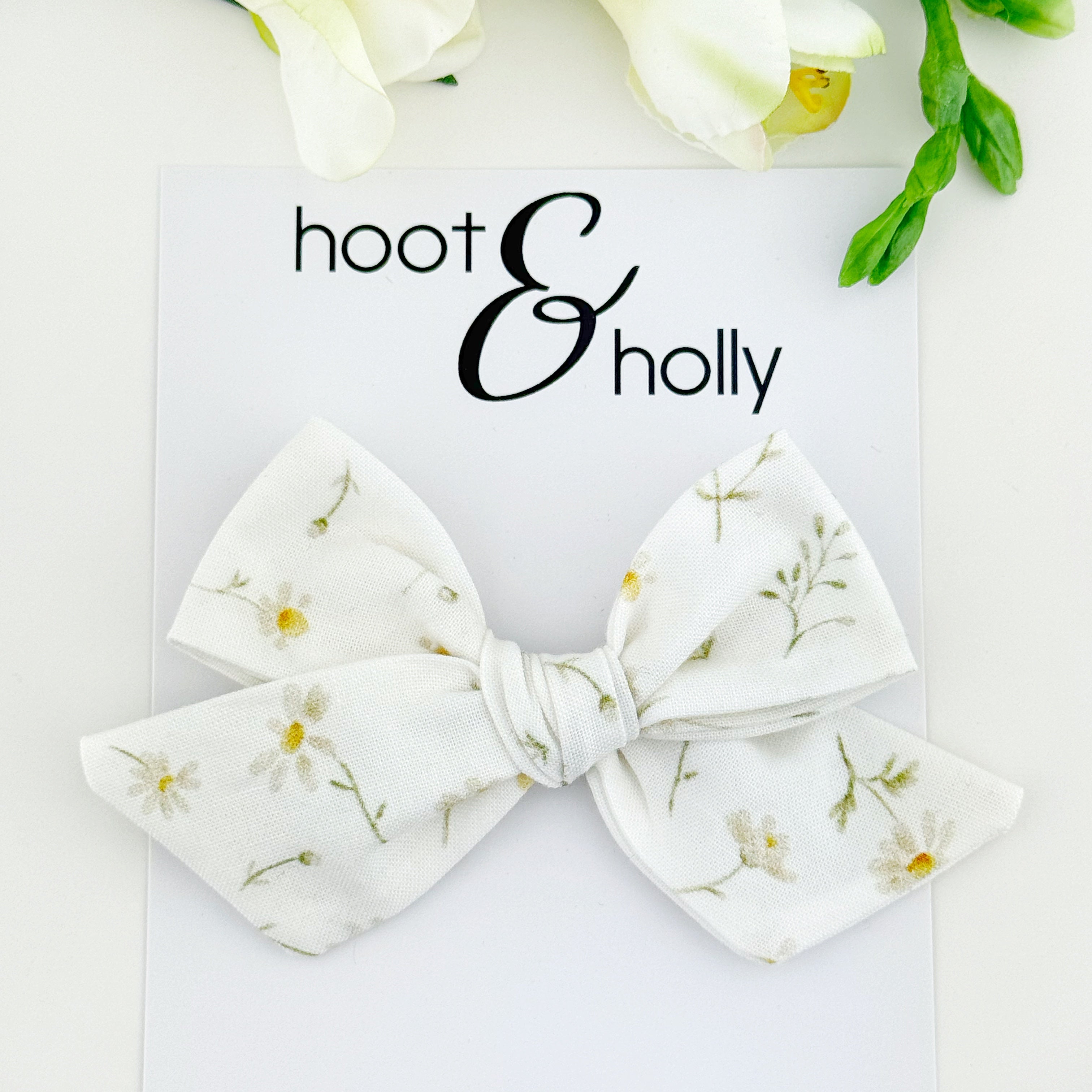 White floral daisy bow with 'hoot & holly' branding on a light background