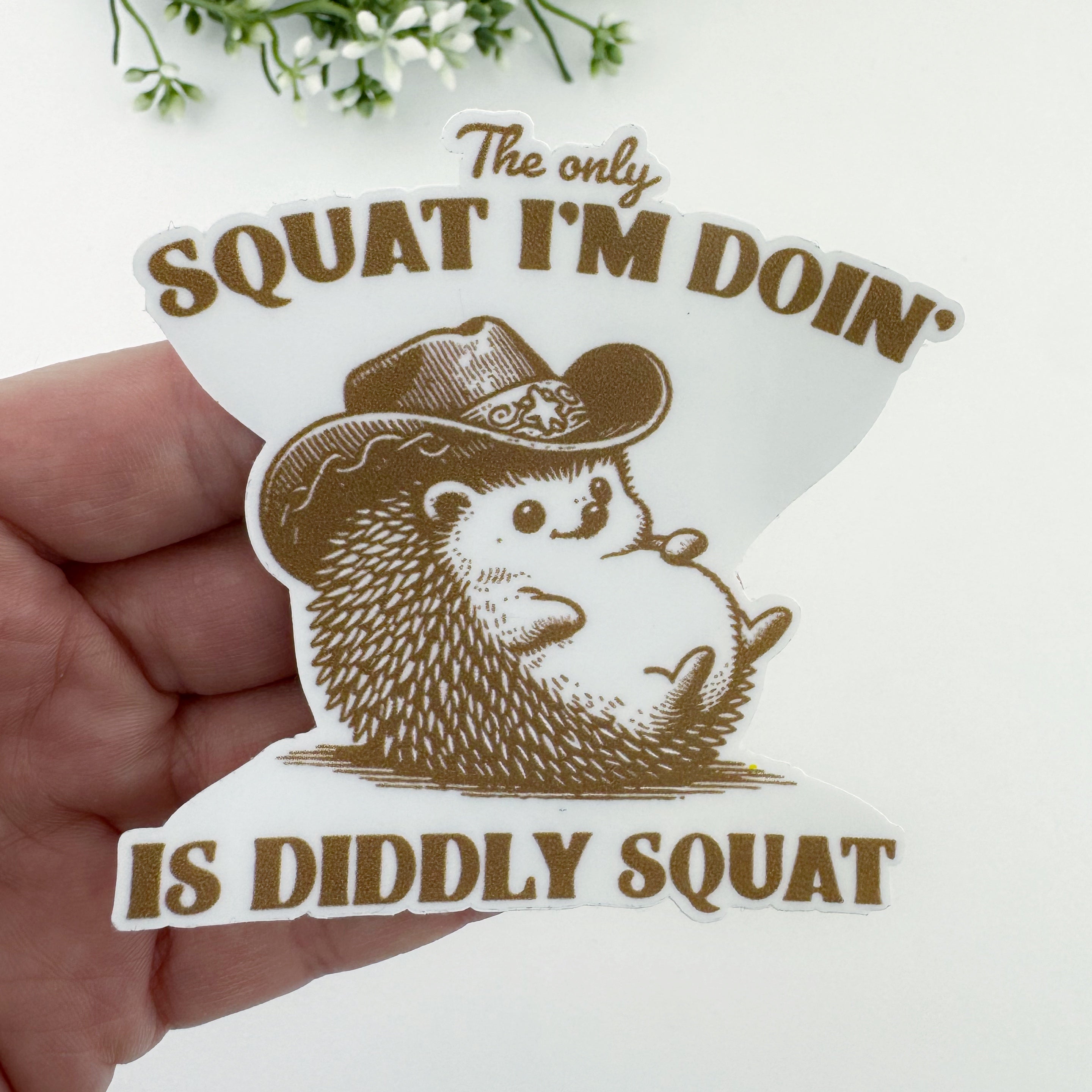 Sticker with a hedgehog wearing a cowboy hat and humorous text. The only squat I'm doing is diddly squat.