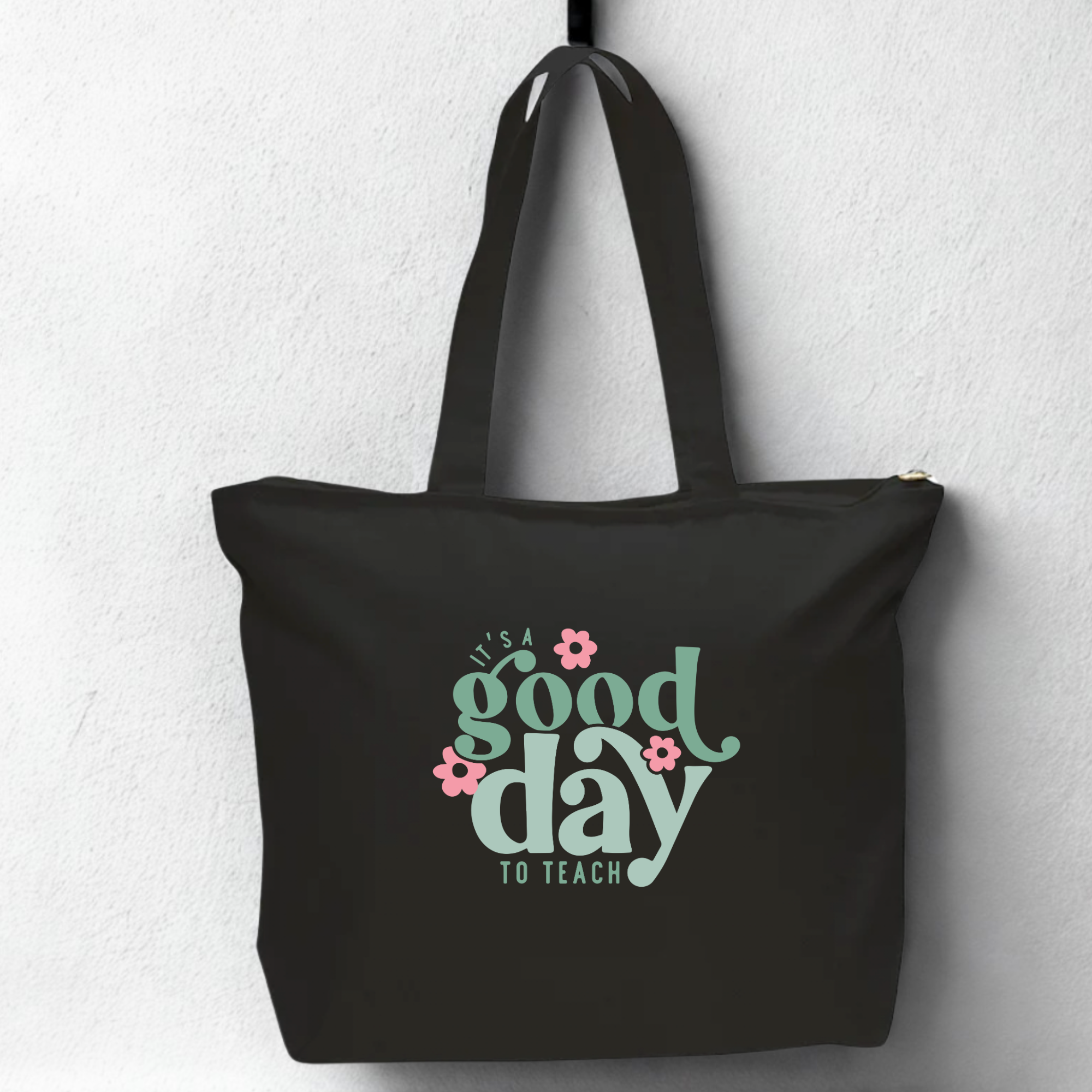 Black tote bag with 'It's a good day to teach' text and flowers on a light gray background