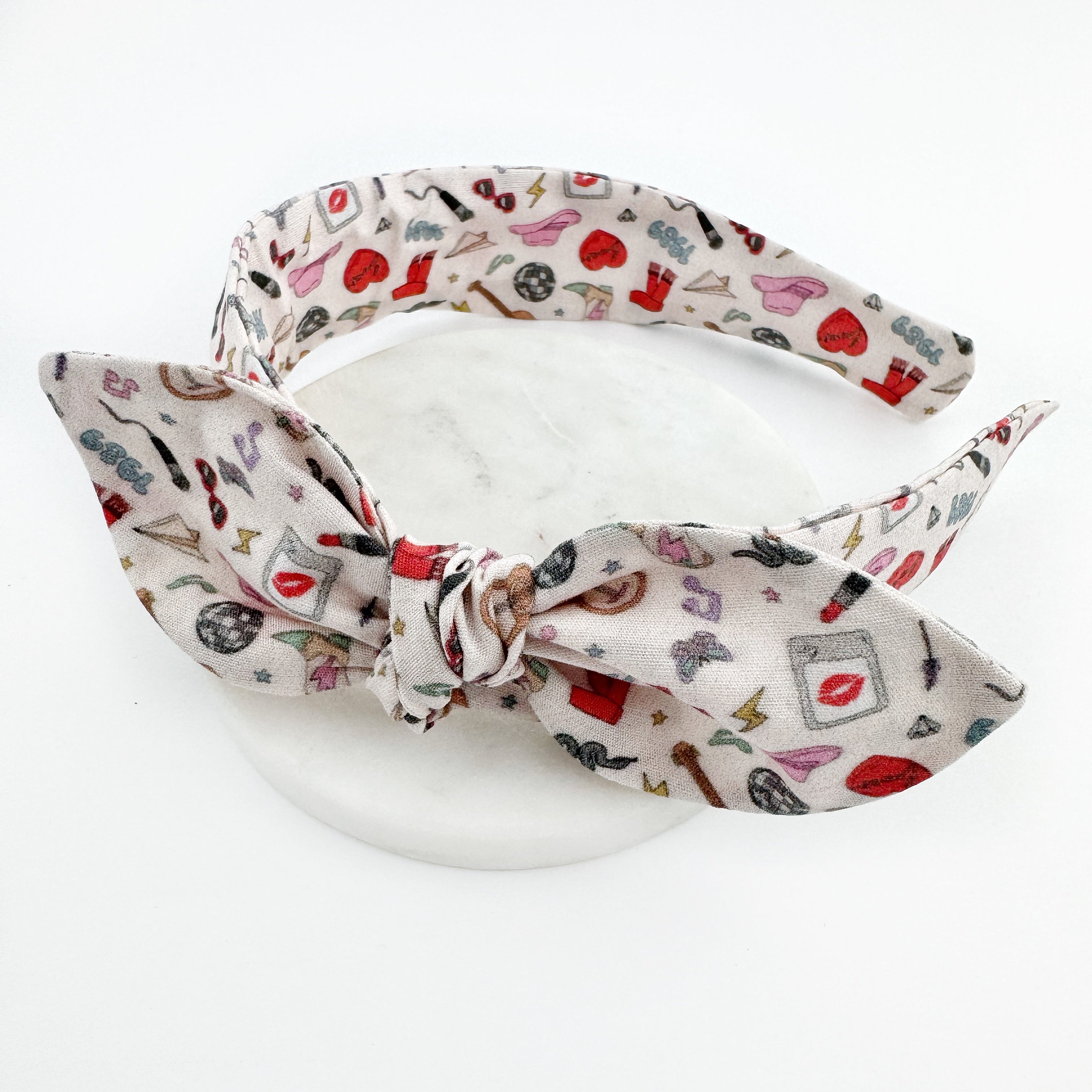 A beige knot bow headband with a Eras Taylor Swift pattern.