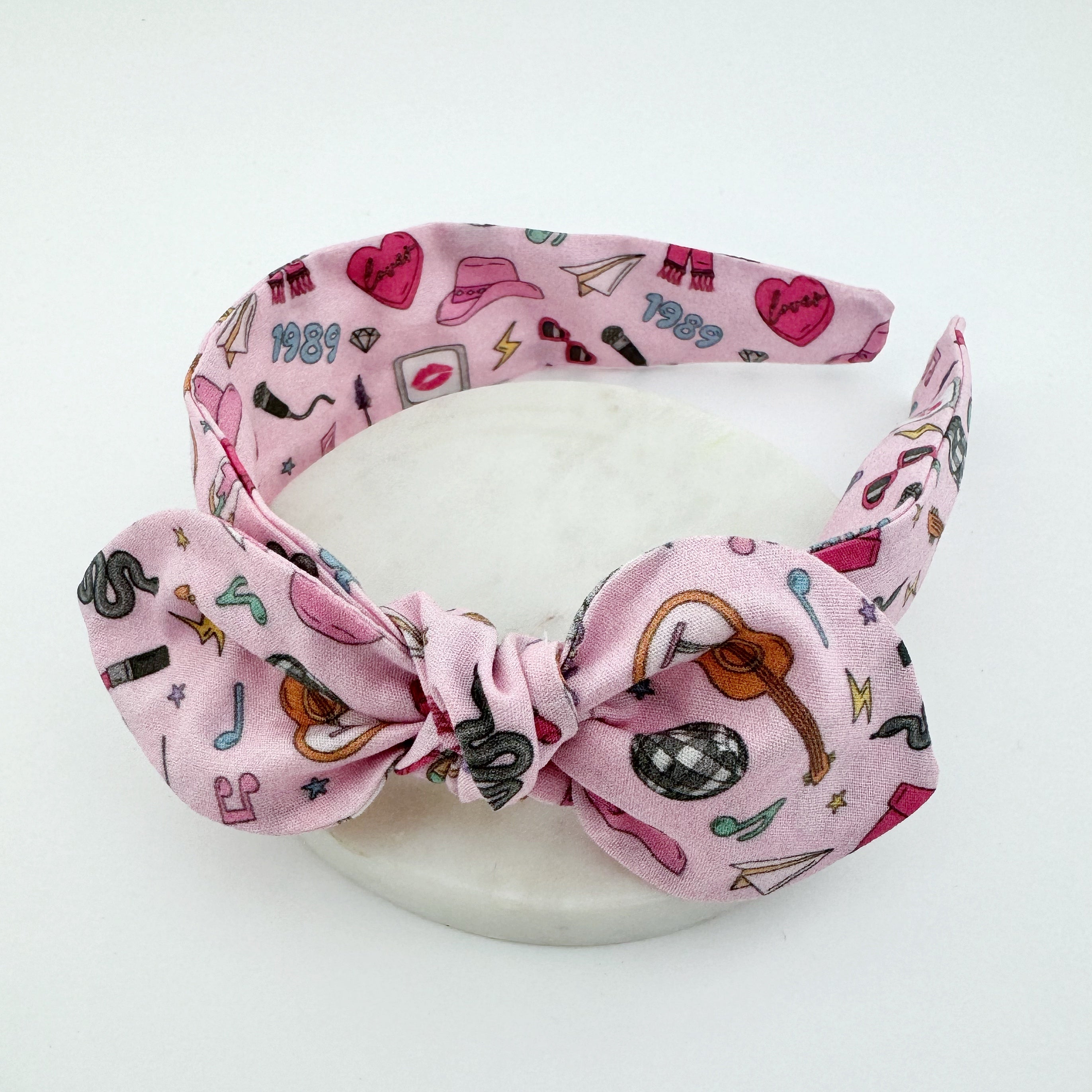 A pink headband with Eras icons, Taylor Swift headband