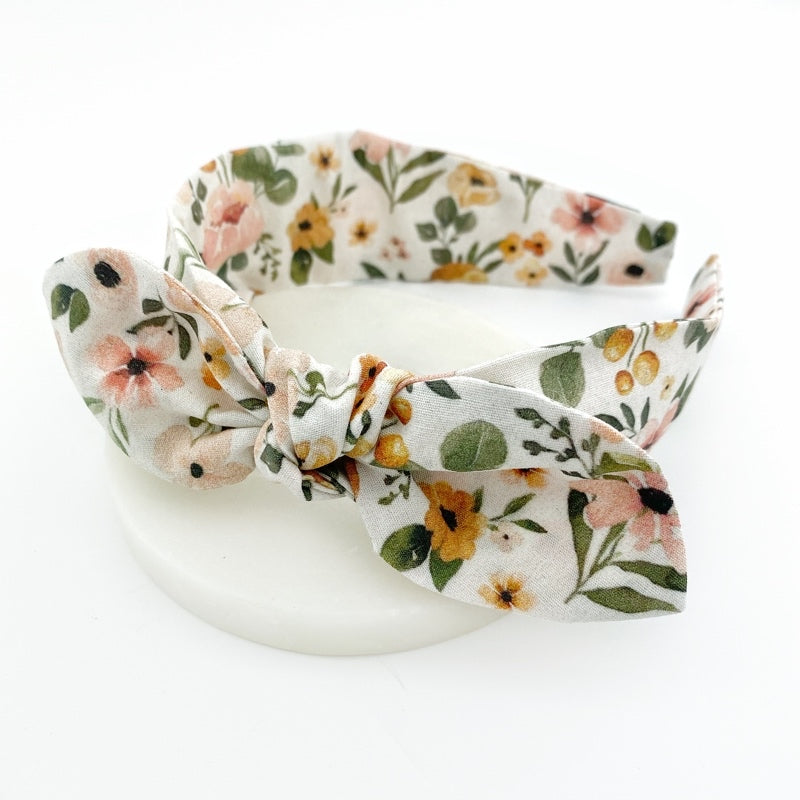 A white knot bow headband with a sunset floral pattern on it, displayed on a neutral background.