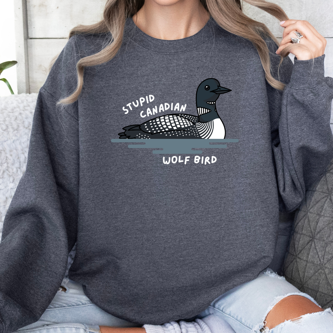 Person wearing a dark gray sweatshirt with a graphic of a bird and text, sitting on a light-colored couch.